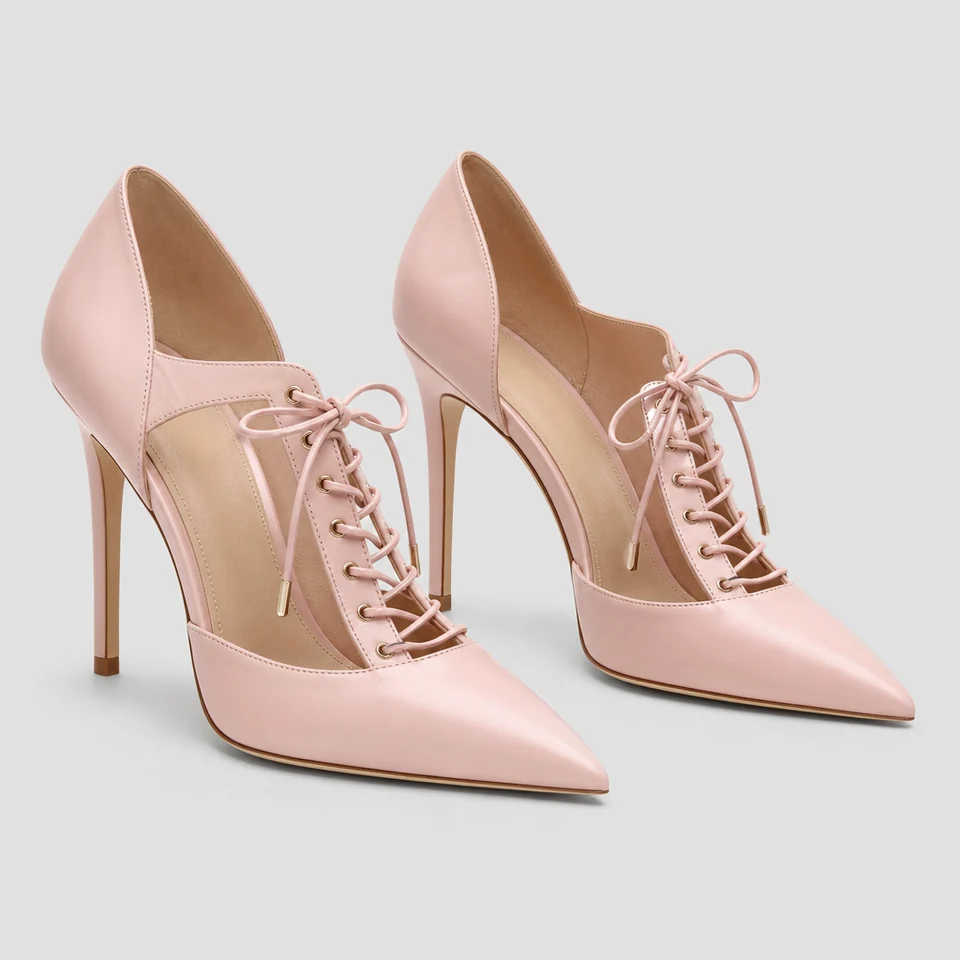 Pair of pale pink pointed toe pumps with lace-up front and high stiletto heels on grey background