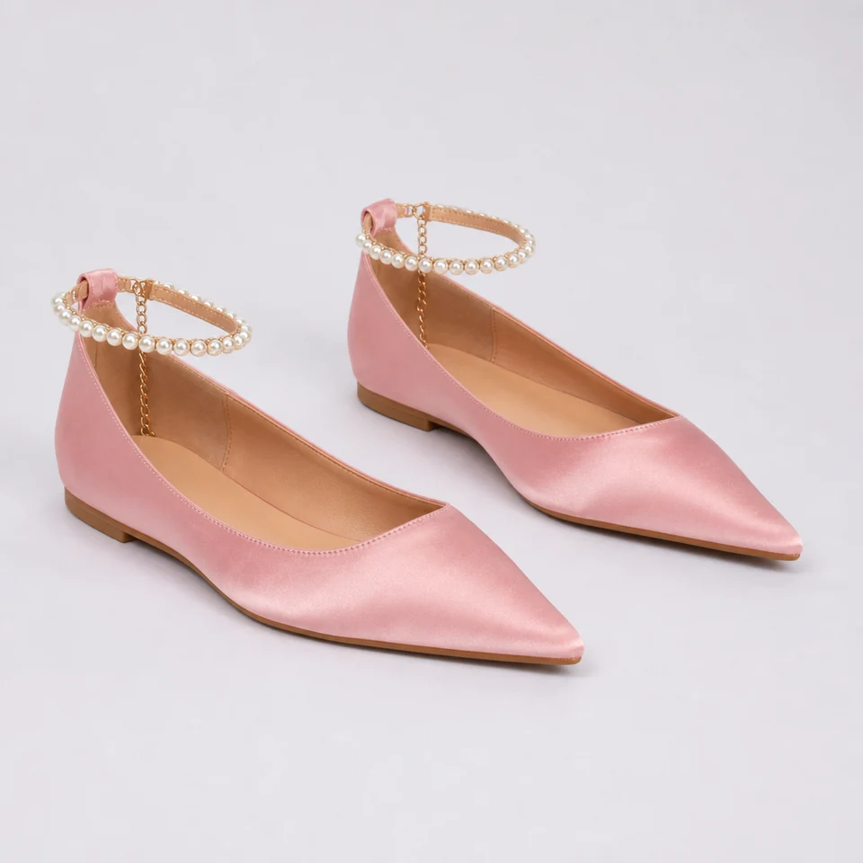 Pair of pink satin-look pointed flats with pearl chain ankle straps on light background